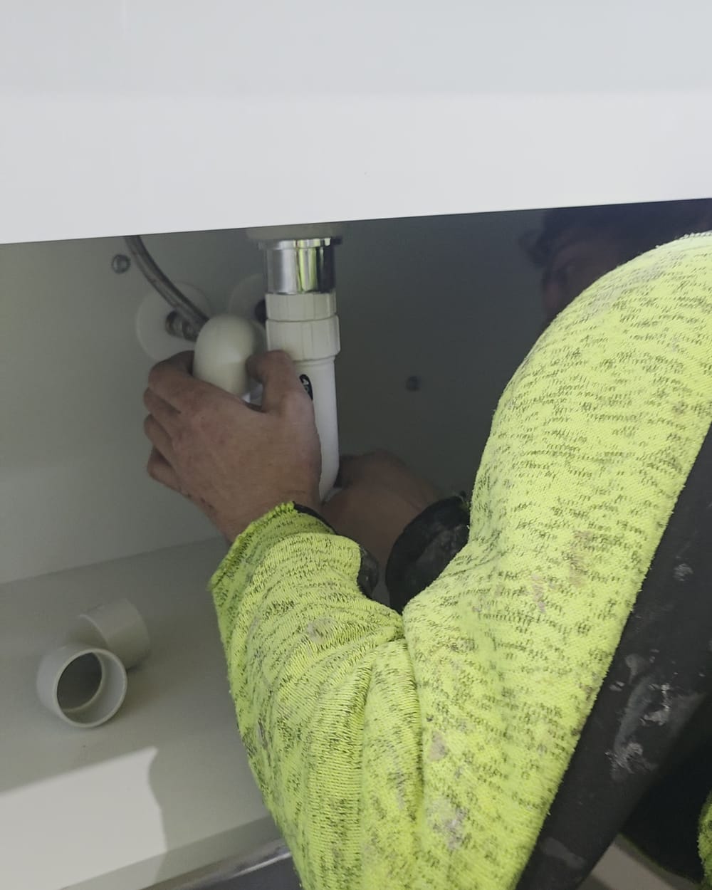Inline plumber fitting the waste and trap beneath a bathroom vanity basin